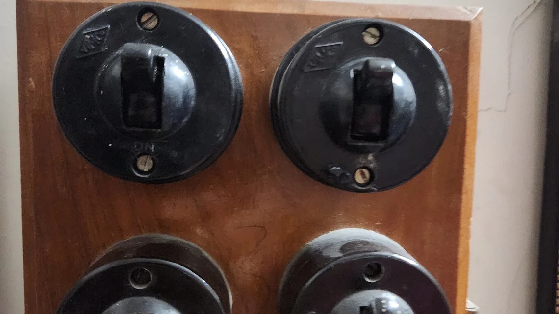 Verniklenmiş ahşap bir levhaya vidalanmış dört eski bakalit anahtar; üstteki ikisinin kolu aşağı bastırılmış.