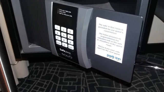Bir otel odasındaki küçük çelik kasa açık duruyor; kapağın iç yüzünde kullanım talimatı ve tuş takımı görünüyor.